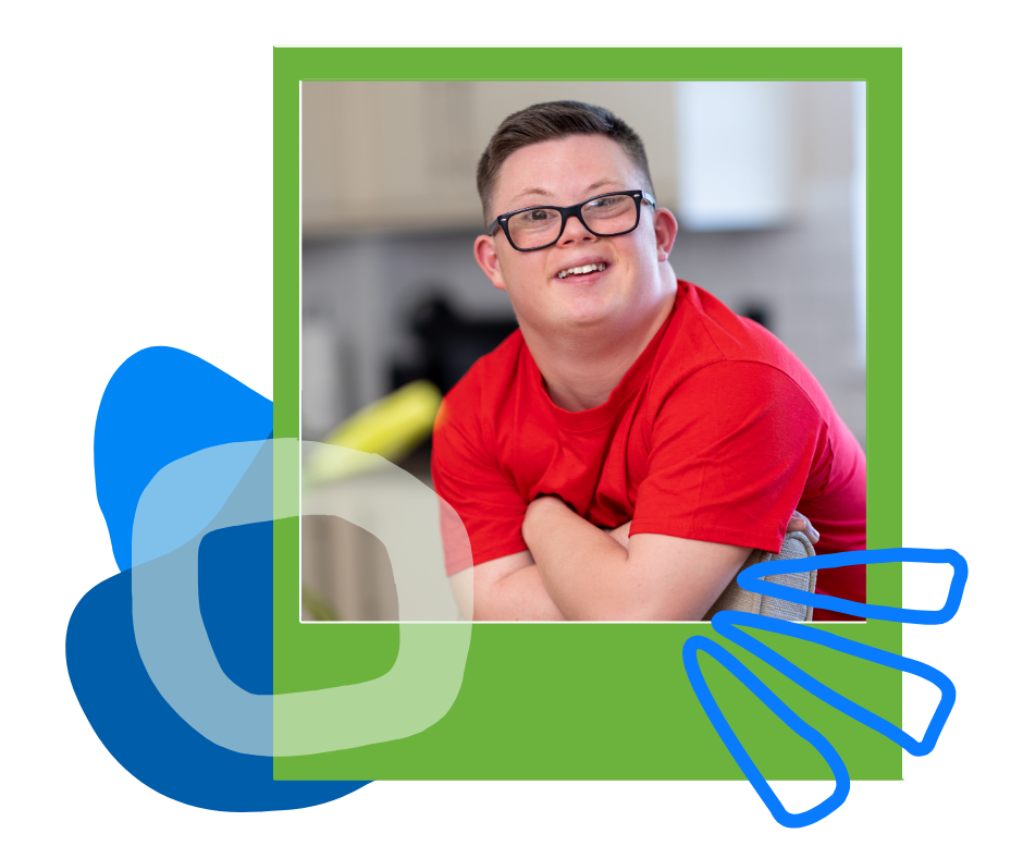 A smiling young man in glasses and a red shirt leaning on a counter