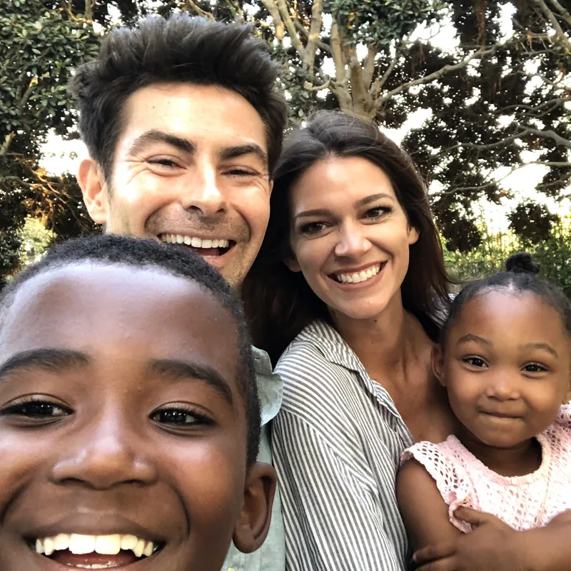ariel-home-get-involved-foster-family-square Two parents and two young children smiling together outdoors in a selfie