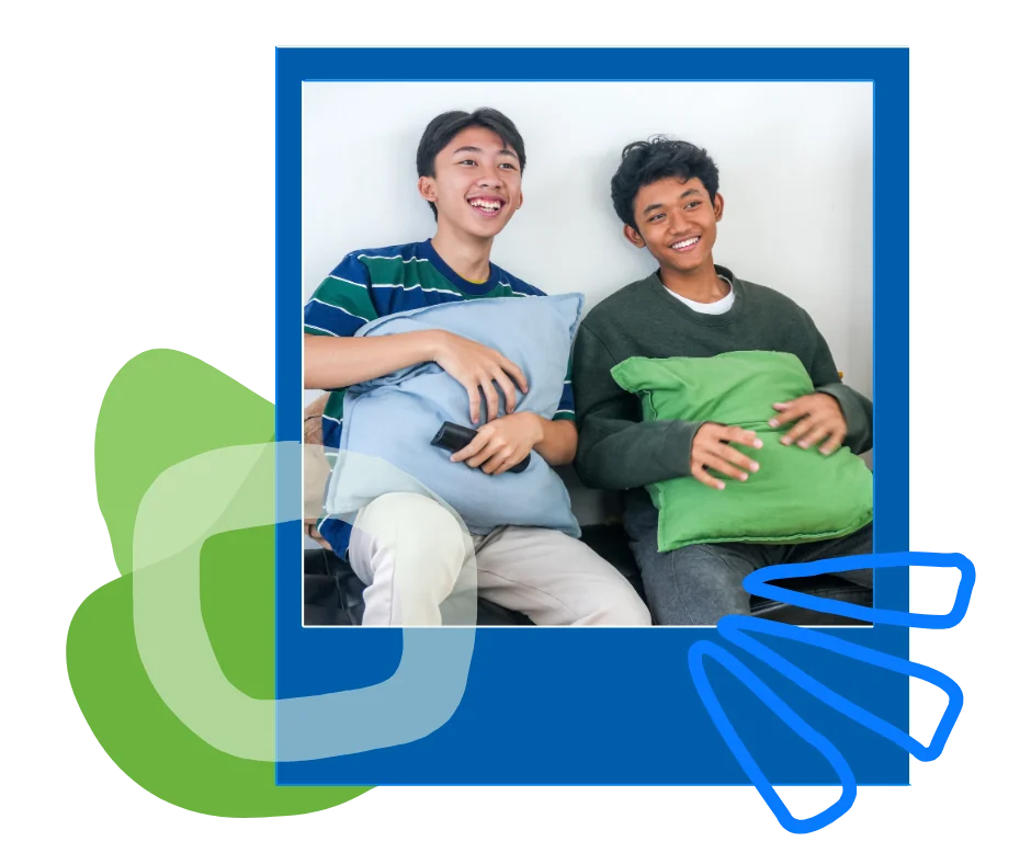Two teenage boys watching tv on a couch, holding pillows