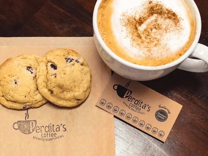 A latte and two chocolate chip cookies beside a Perdita's Coffee bag and punch card