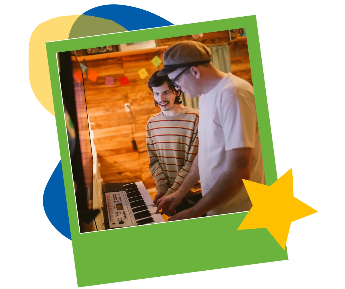 Two men play a keyboard together in a warm, wood-paneled room.